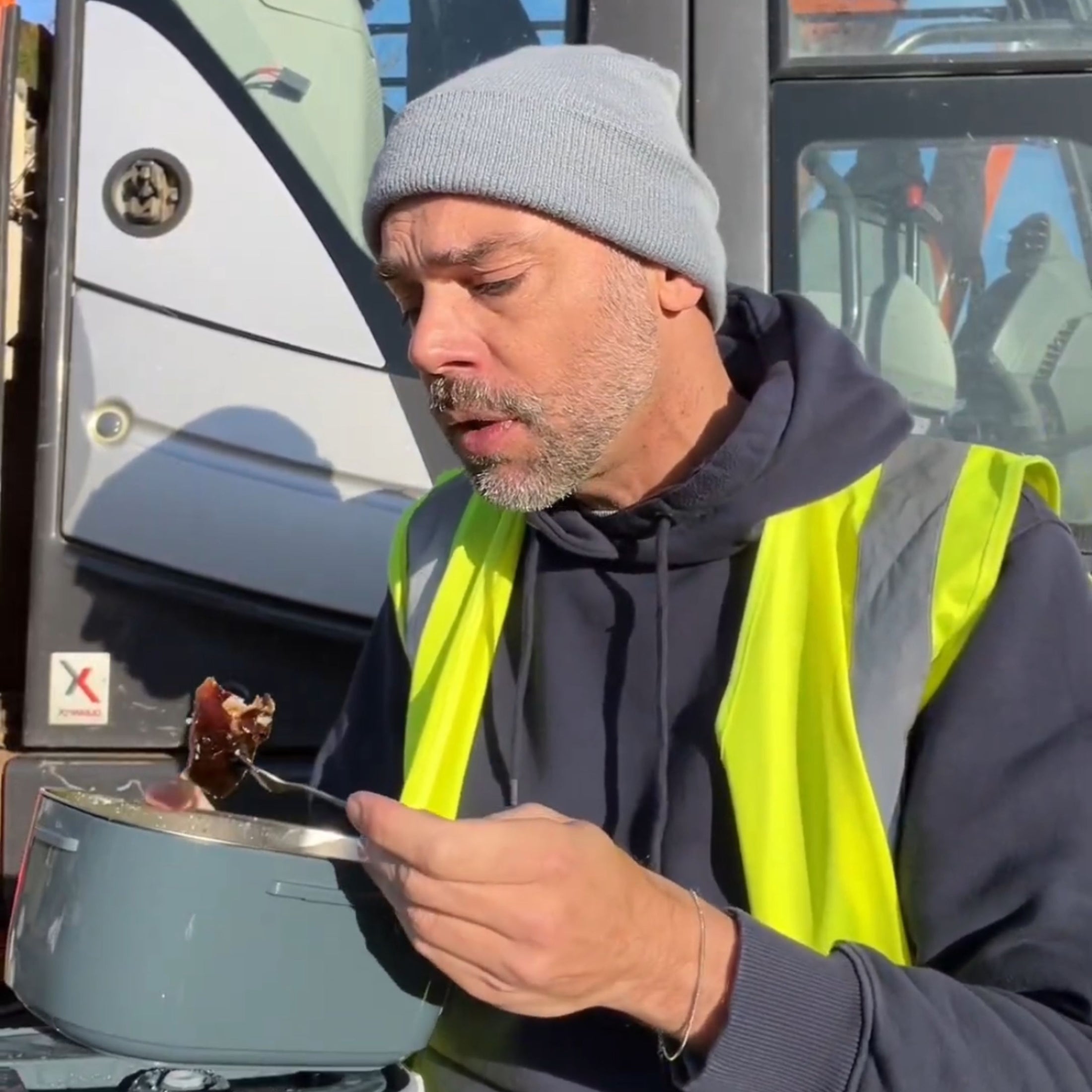 Man in a high-visibility vest eating from a electric lunch box 