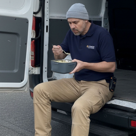 Man sitting in the back of a van eating from a bowl.