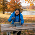 Load image into Gallery viewer, Person eating from a Portagrub, electric lunch box, on a wooden picnic table in an autumn park.
